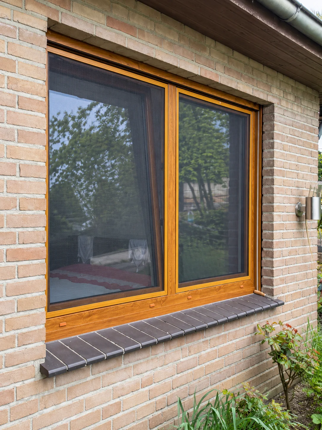 Insektenschutzrahmen an einem zweiflügeligen Holzfenster in einer Backsteinfassade